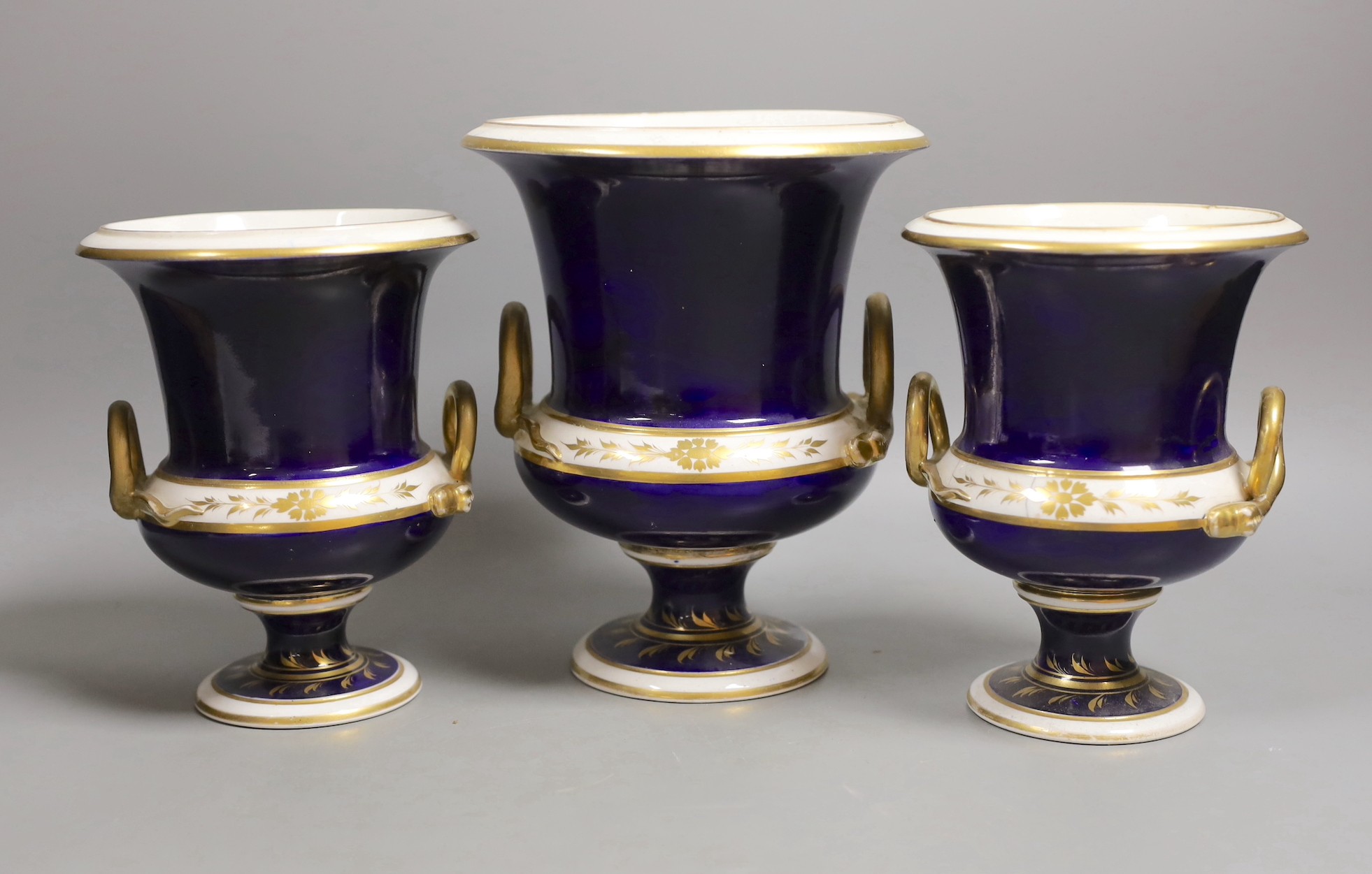 A garniture of three Derby named twin handled cups, View near Belper, Derbyshire, and 'View in North Wales' and 'View near Rome', 17cm and 20.5cm